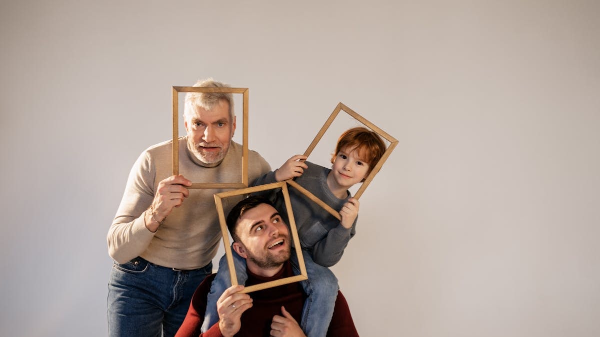 A joyful family portrait featuring grandfather, dad, and child posing with wooden frames in a studio setting.