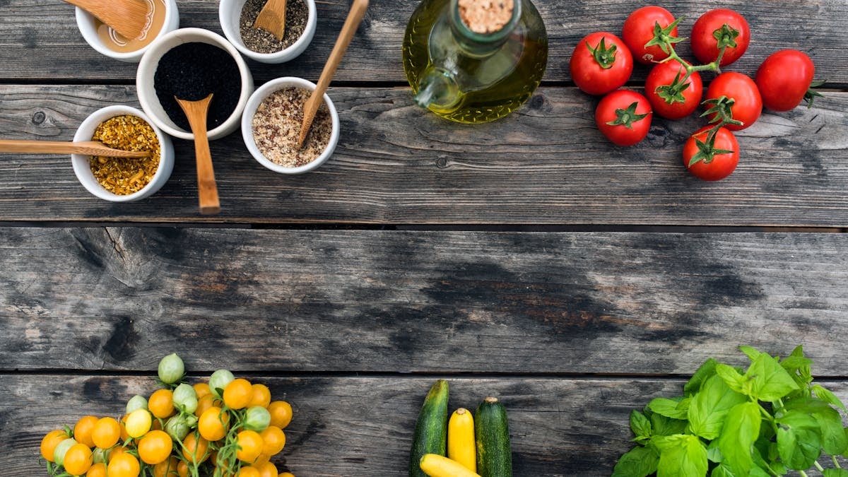 Top view of fresh vegetables and spices for salad placed on wooden table in daytime